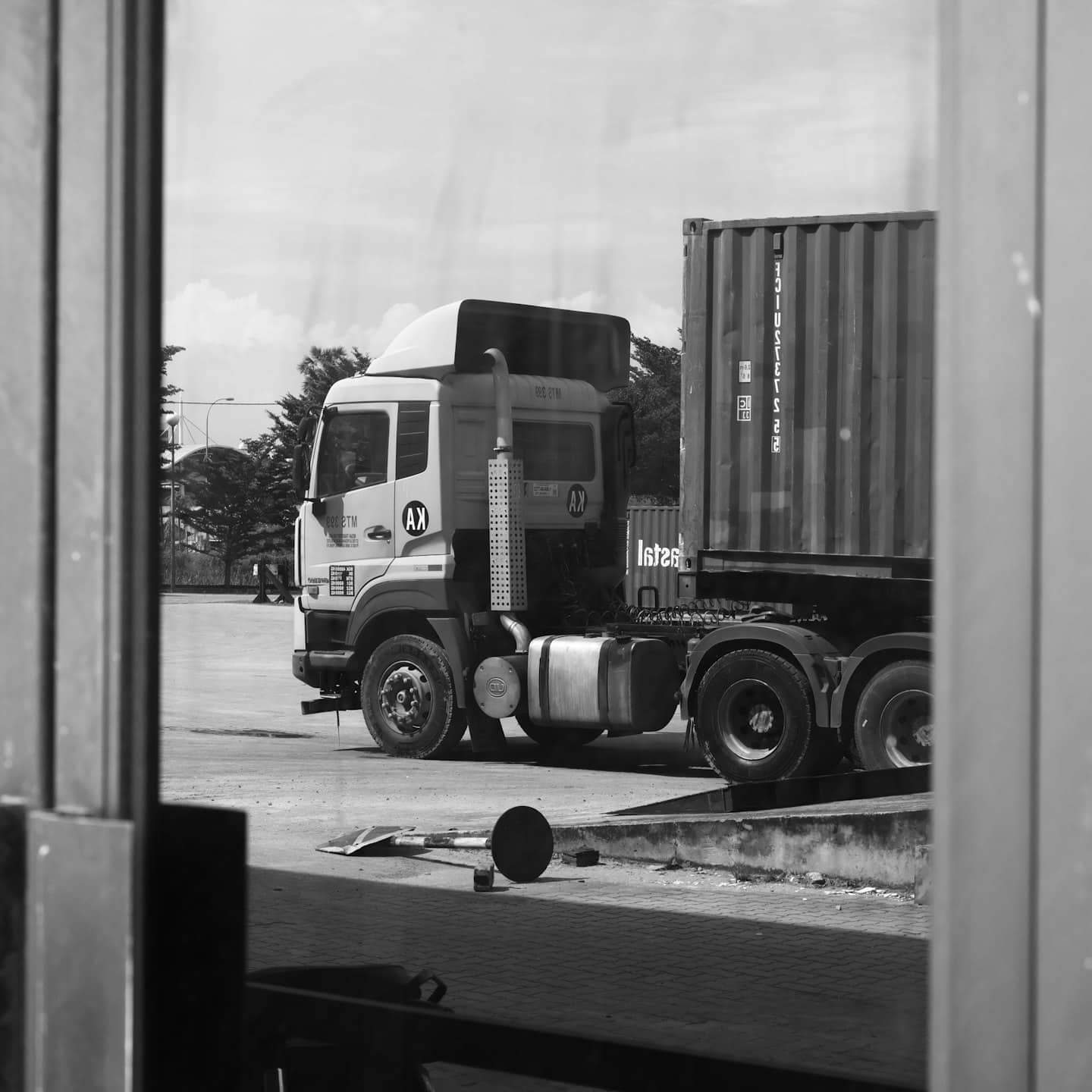Biała ciężarówka z logo firmy logistycznej zaparkowana na utwardzonym placu.