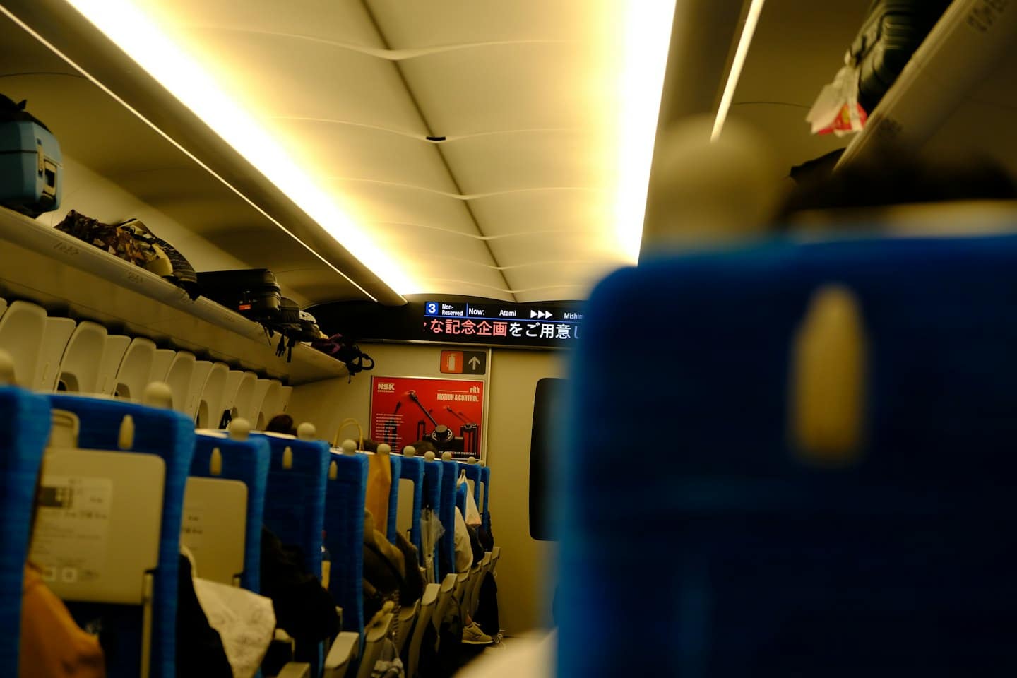 Pasażerowie siedzą na niebieskich siedzeniach w nowoczesnym wagonie kolejowym.