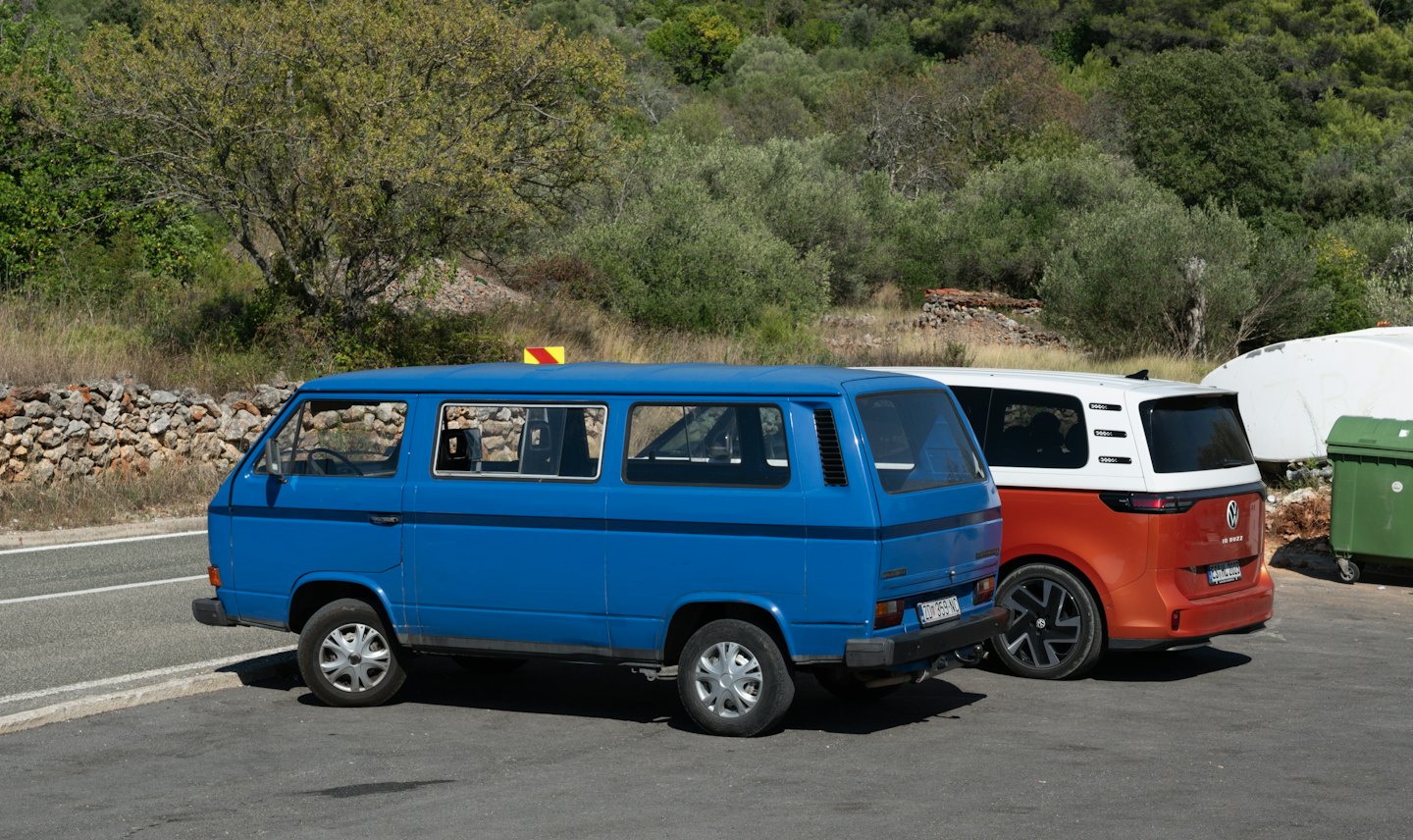 Niebieski VW Transporter T3 i pomarańczowy ID. Buzz zaparkowane na asfalcie.